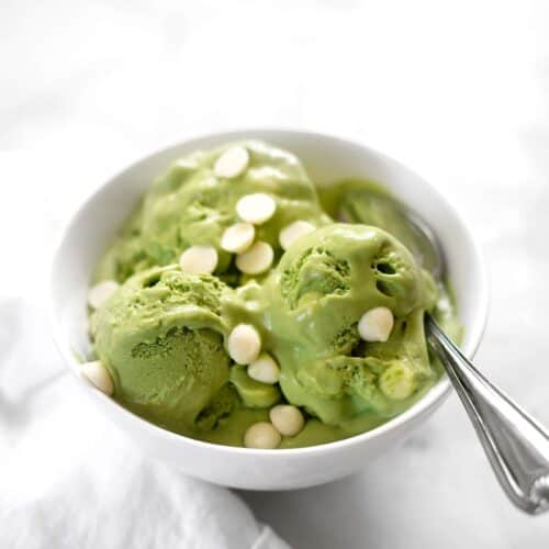 green, Dairy Free Matcha Ice Cream in a white bowl with a spoon... visible white chocolate chips sprinkled on top
