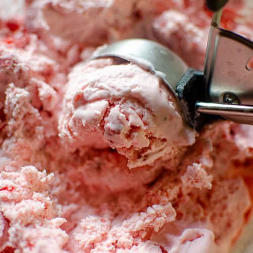 a scooper dipping into a tub of homemade strawberry ice cream