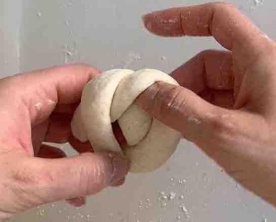 hands tucking one end through the hole in the dough rope to tie a knot