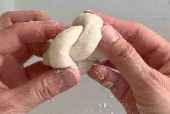 hands tucking ends of dough rope under the knot 