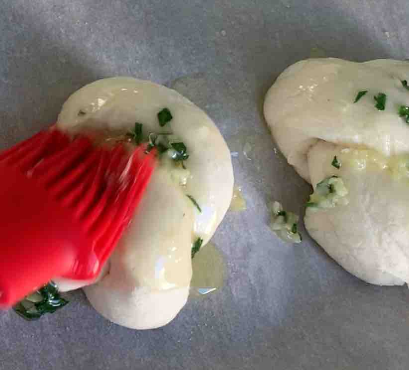 gluten-free garlic knot being coated with garlic, parsley butter with a red silicone pastry brush