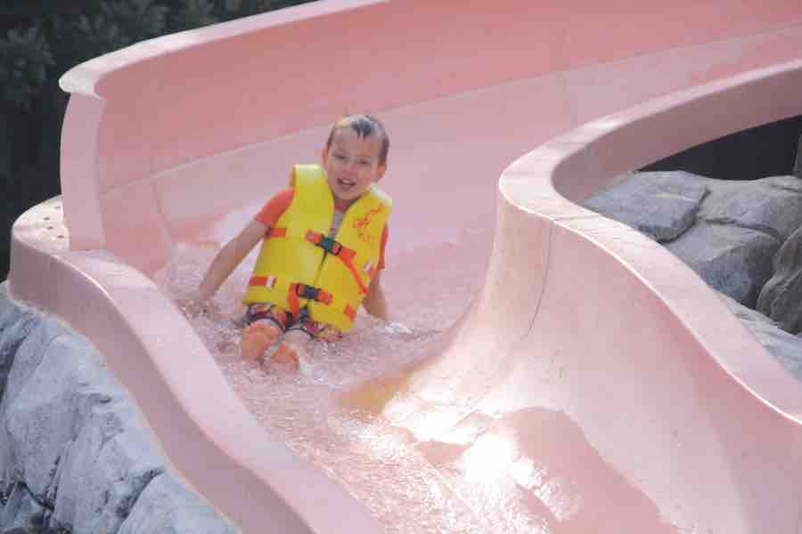 CJ coming down a light orange/pink water slide