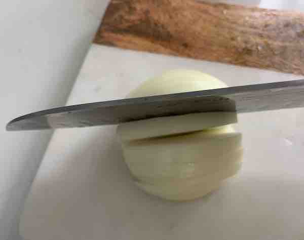 a large knife slicing half an onion, resting on a marble and wooden cutting board