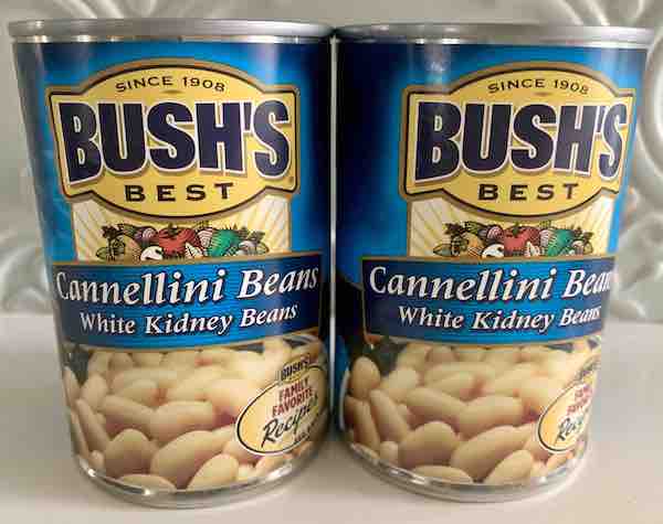 two cans of Bush's Cannellini Beans on a white counter
