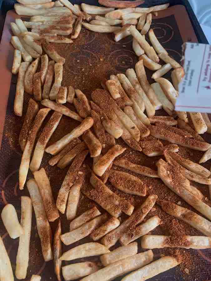 cooked French fries on a baking sheet, being sprinkled with taco seasoning
