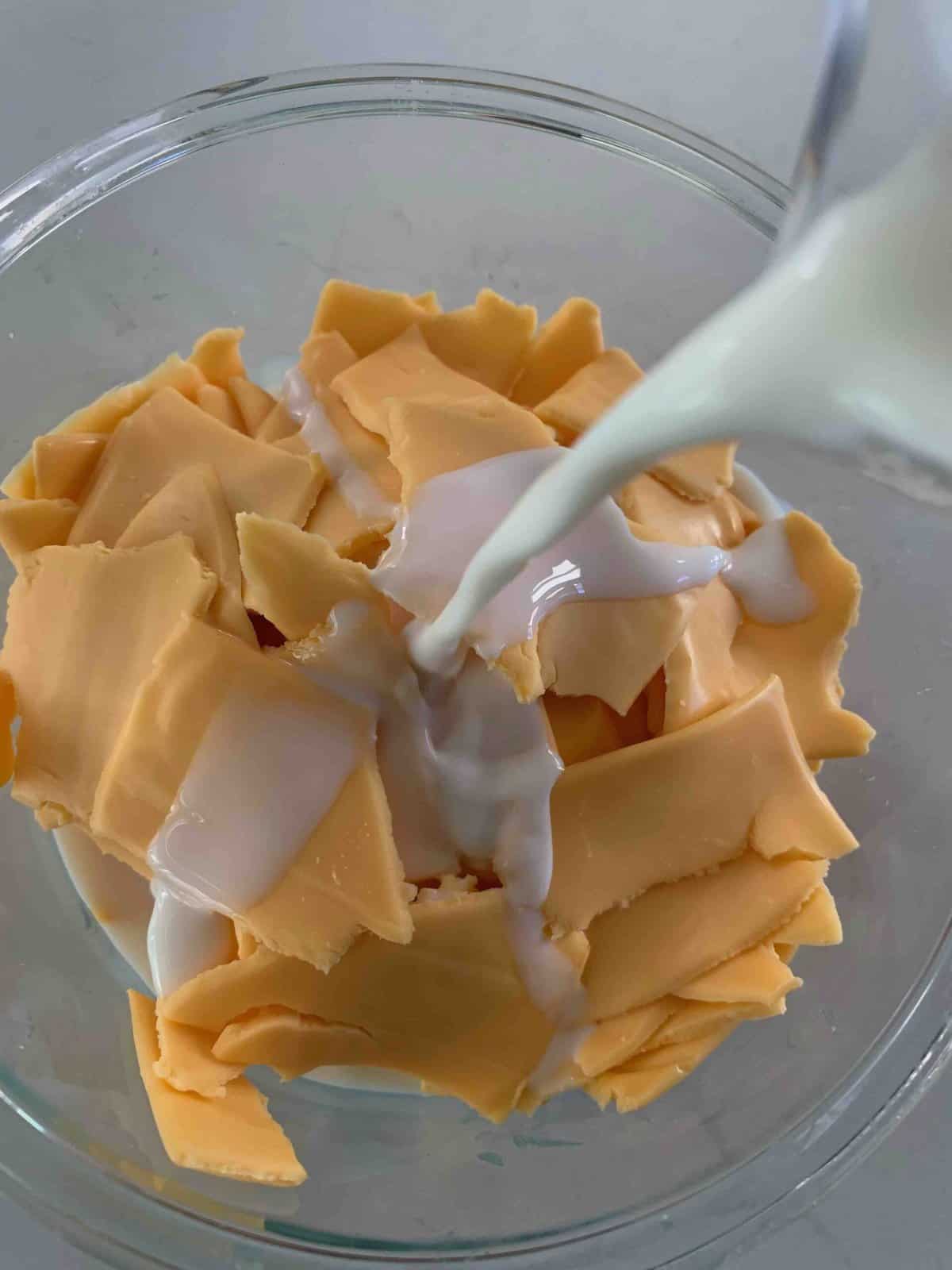 top view of milk being poured into a bowl of broken pieces of American cheese