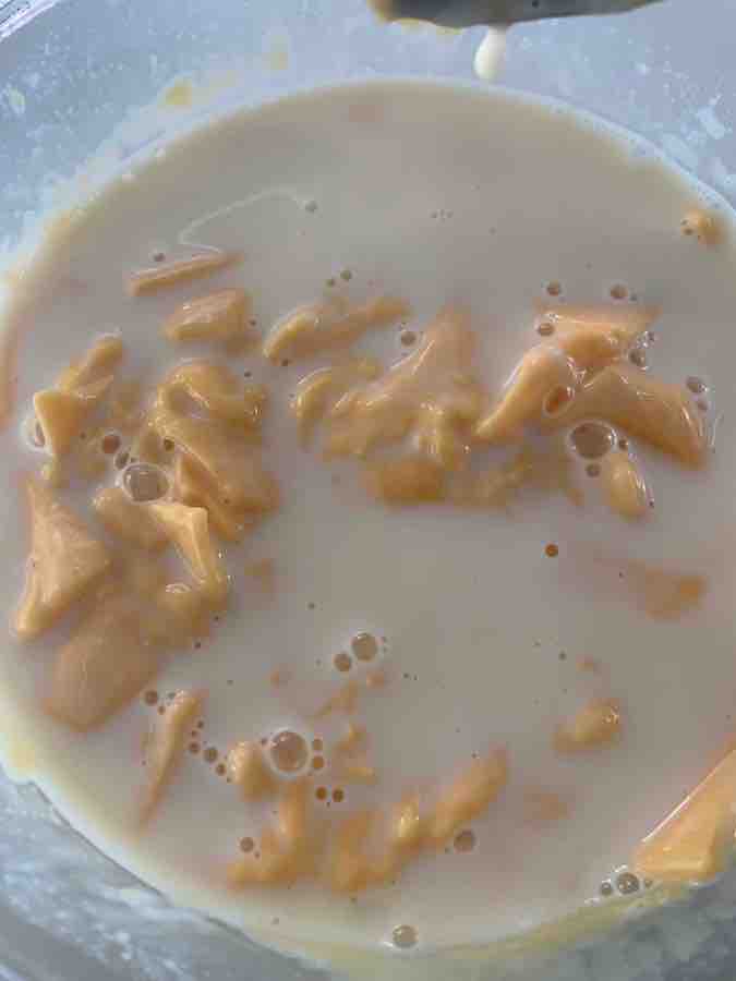 bowl of American cheese pieces partially melted into the milk, still very clumpy