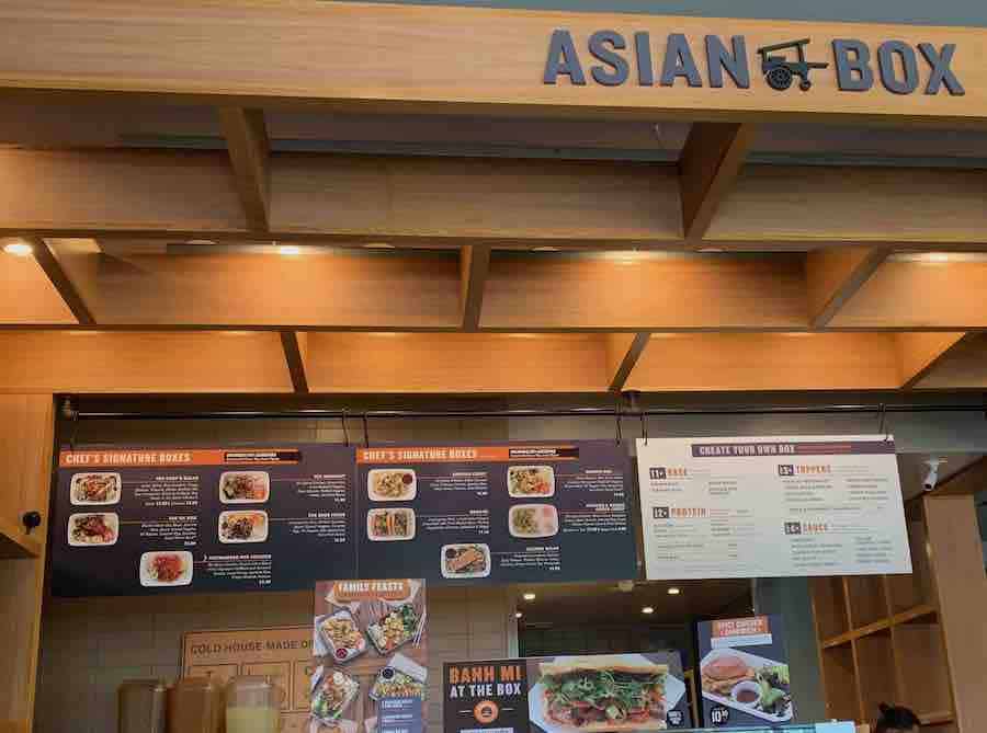 Inside Asian Box Restaurant... sign with "Asian Box" name above the order counter, display menu board with choices of gluten-free boxes, photo of Bahn mi sandwich on counter below, kitchen in background