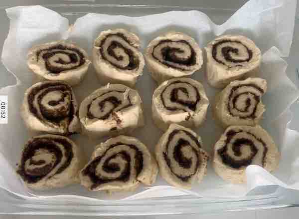 overhead view, a glass baking pan covered with parchment paper and filled with 12 gluten-free cinnamon roll dough pieces, before rising, space between rolls