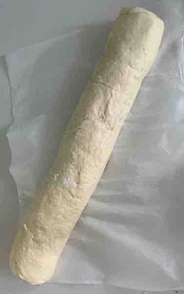 fully rolled log of  the long edge of gluten-free dough on white parchment paper