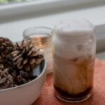 apple crisp macchiato in a mason jar, next to a bowl of pinecones