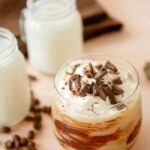 chocolate frappuccino in a short glass with chocolate drizzle visible on the glass, lighter colored frap topped with whipped cream and chocolate shavings