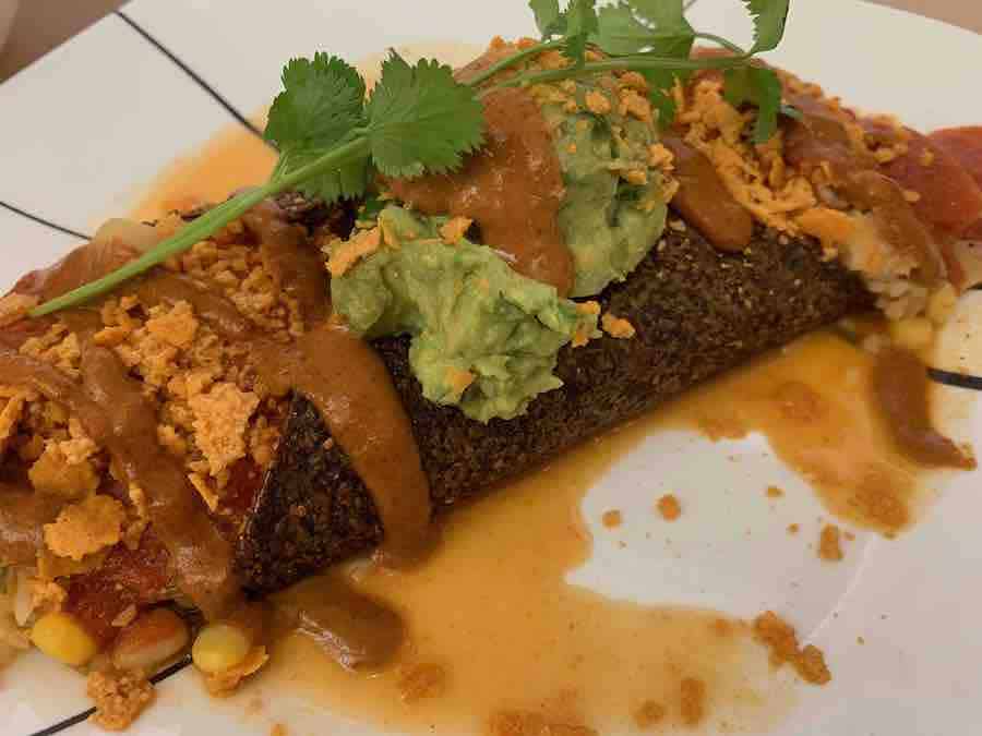 a gluten-free vegetarian enchilada with sauce, guacamole and cilantro on top