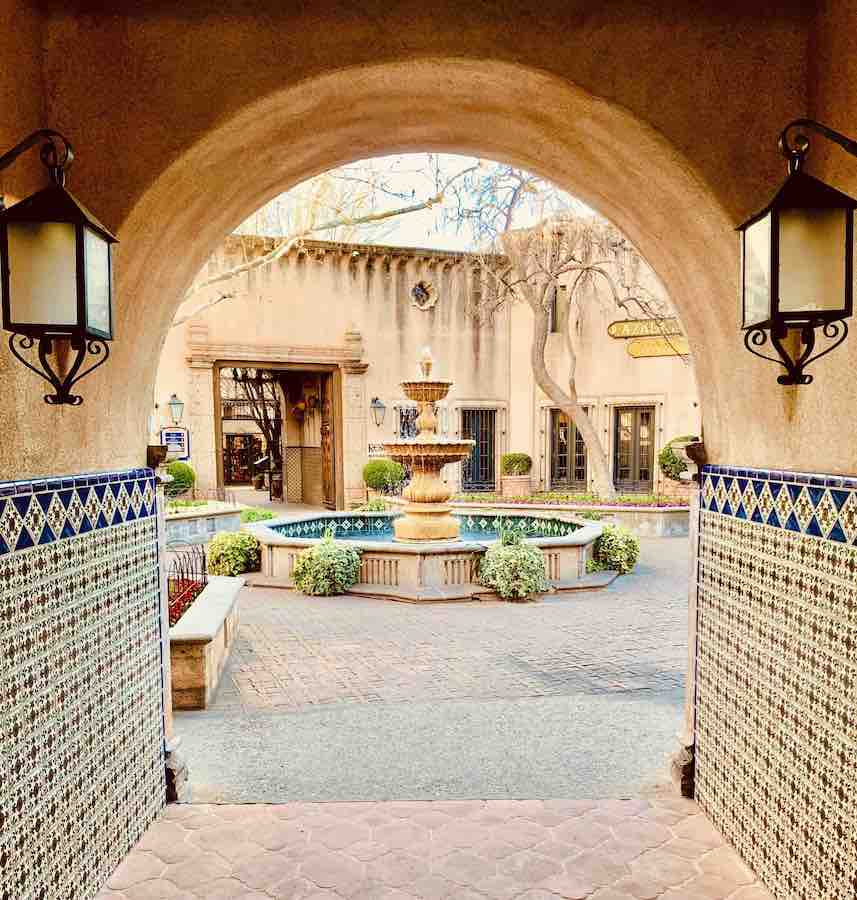 Spanish-style archway with tiles along the wall, and a view of a courtyard and large fountain on the other side