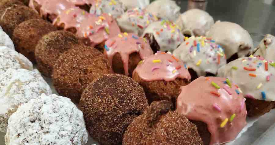 rows of gluten-free donut holes, first row is powdered sugar, then cinnamon sugar, pink frosting with sprinkles, white frosting with sprinkles, and white frosting