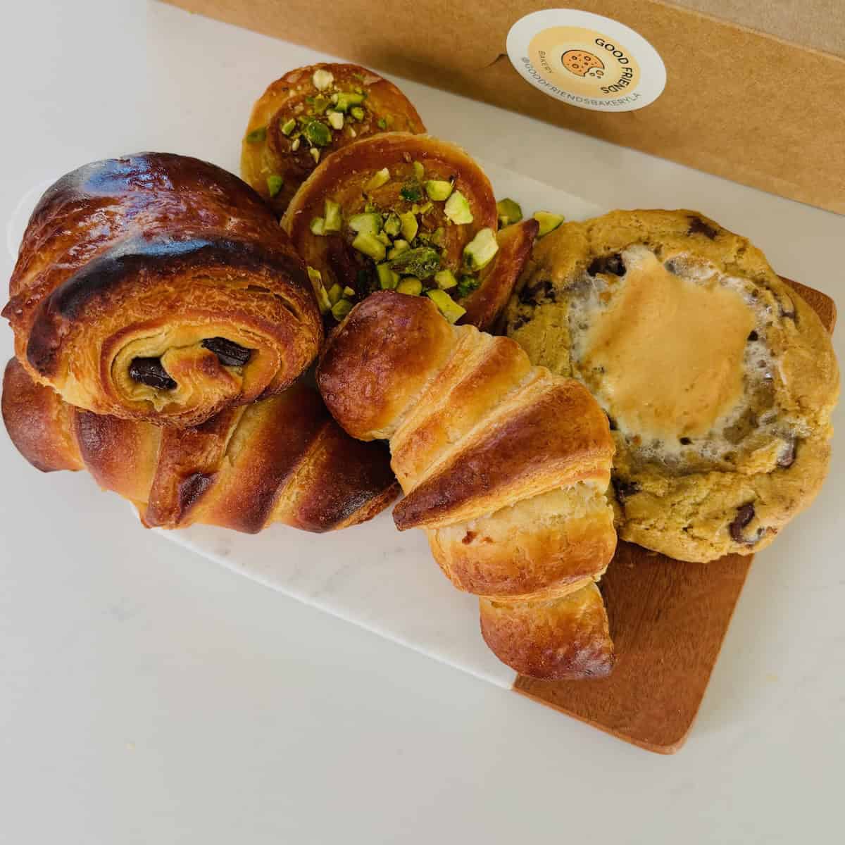 Croissants, Pain au chocolat, pistachio pinwheels, and a giant store cookie on a cutting board