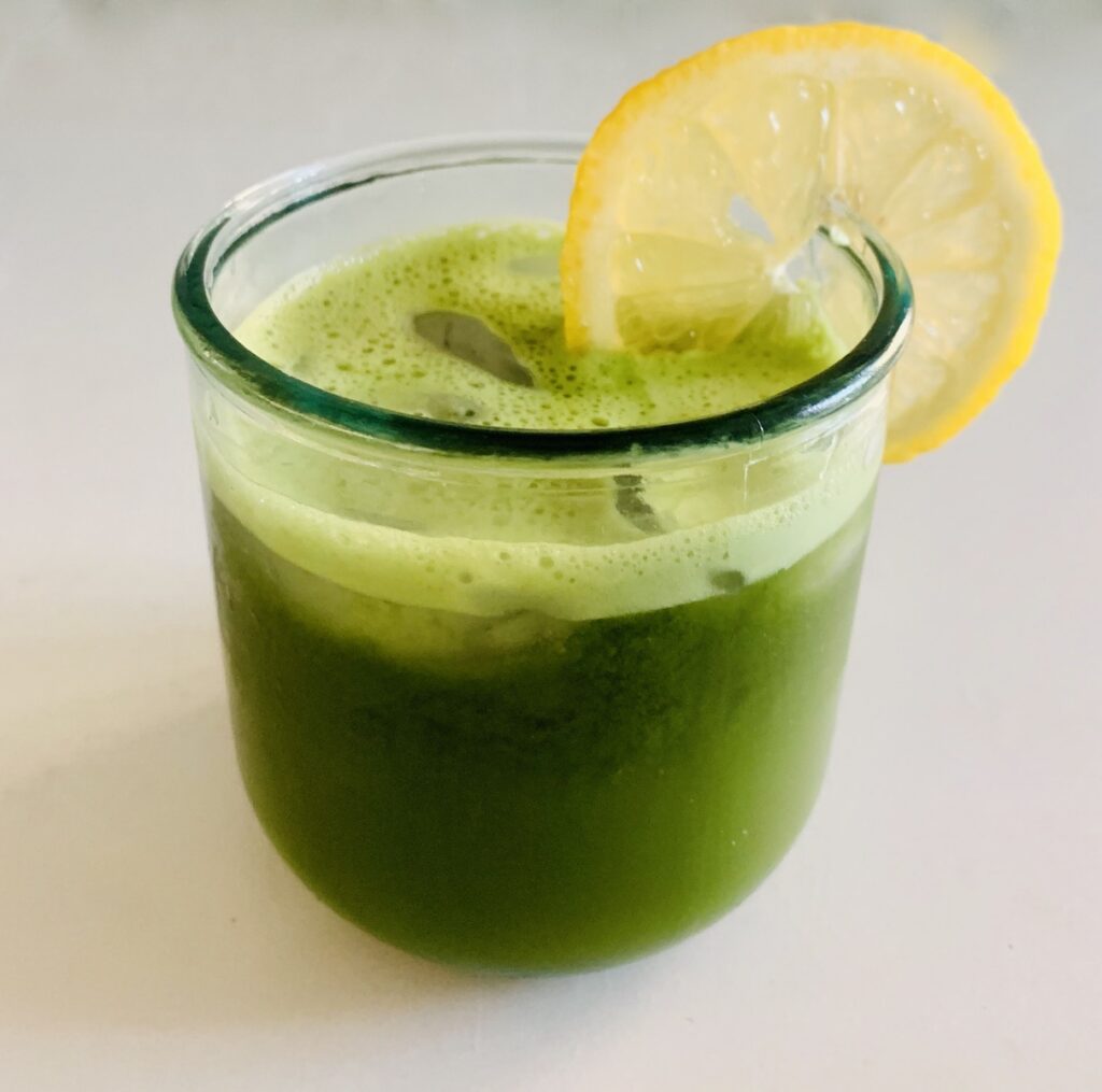bright green matcha lemonade in a glass of ice with a lemon slice on the rim, sitting on a white counter