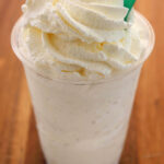 vanilla bean Frappuccino with whipped cream topping in a clear plastic cup and a green straw