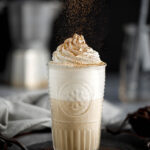vanilla coffee Frappuccino in a glass with visible layers of caffe-colored frap, white, and topped with whipped cream