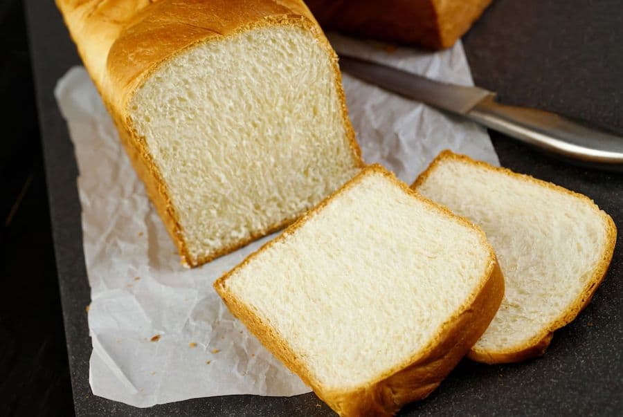 homemade loaf of bread on parchment paper, with two slices cut and lying in front and a knife to the side