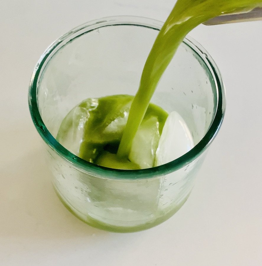 bright green matcha lemonade being poured into a glass of ice