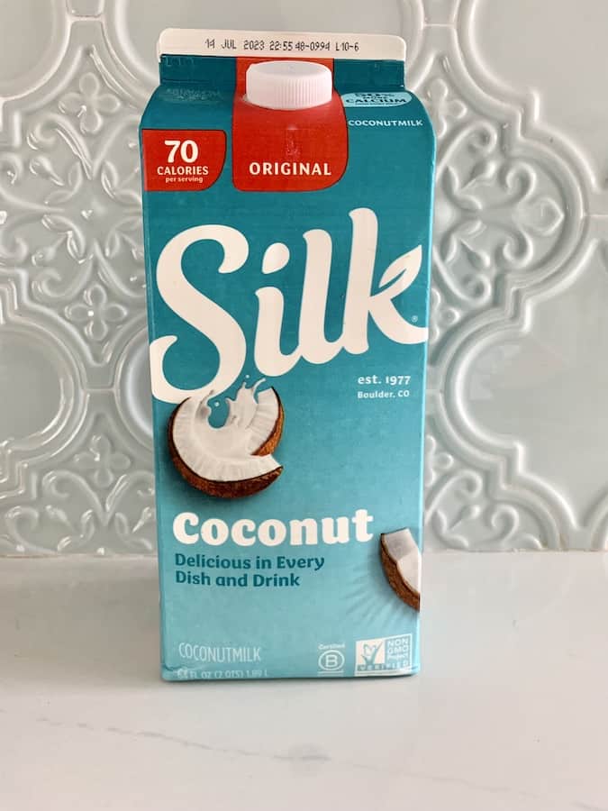bright, aqua-blue carton of Silk Original Coconut Milk sitting on a white counter with light blue tile backsplash