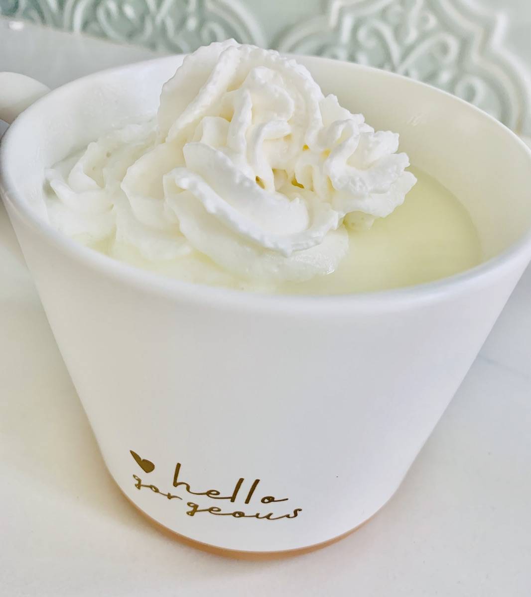 white hot chocolate topped with whipped cream, in a white cup with writing: small heart and cursive text: hello gorgeous