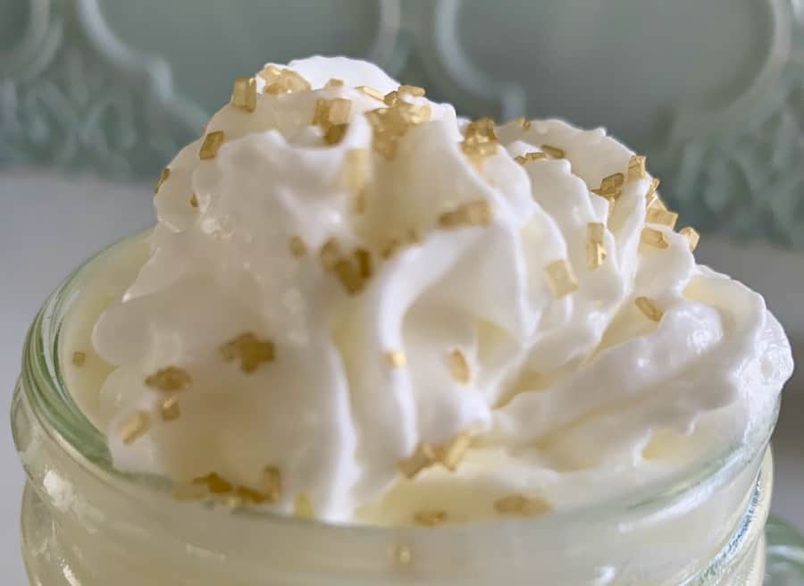 top of a glass mug, you can't see the beverage, but it's topped with whipped cream and gold sprinkles