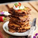 a stack of bacon zucchini fritters on a tiny white plate, topped with sour cream and herbs