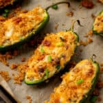 jalapeno halves filled with cheese and topped with bacon, on a baking sheet