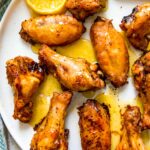 seasoned chicken wings on a white plate with dripping sauce and sliced lemons