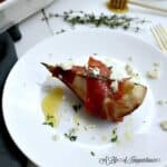 a proscitto wrapped pear on a white plate