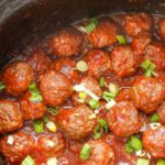 a crockpot full of mini meatballs in cranberry-based sauce
