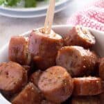 pieces of sausage with a glaze in a bowl, one toothpick in one of the sausage pieces