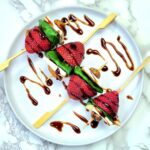 four strawberry skewers drizzled with balsamic on a white plate
