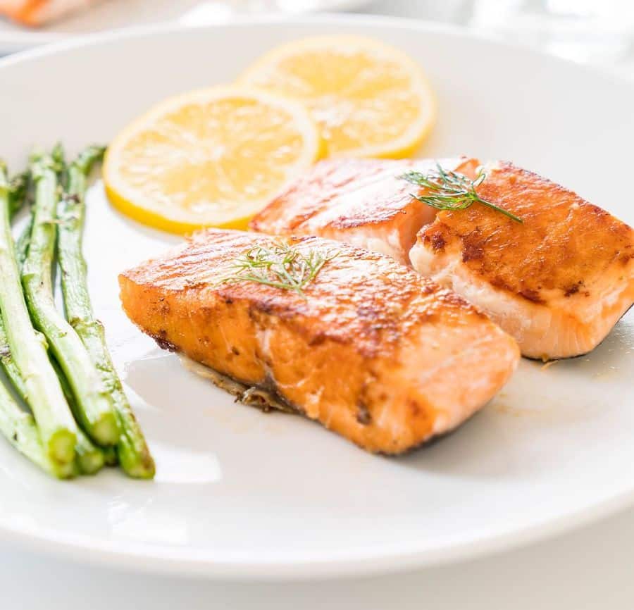 two pieces of salmon, asparagus and two slices of lemon on a white plate