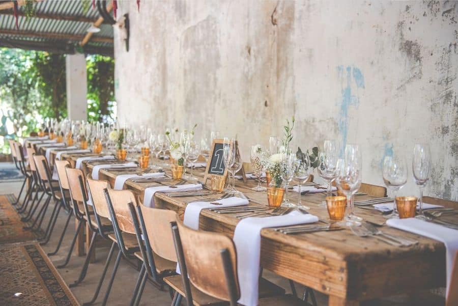 rustic wedding table set up with napkins draping down, wooden farm table, old wall in the background