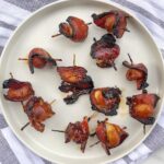 bacon wrapped water chestnuts with toothpicks scattered on a white plate