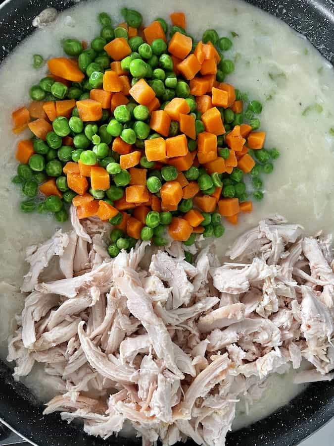 pile of peas and diced carrots and a pile of shredded chicken sitting in a creamy sauce in a pan