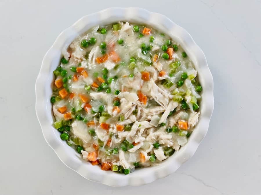chicken pot pie filling with visible chicken, vegetables and creamy sauce in a ceramic pie pan with white fluted edges, top view