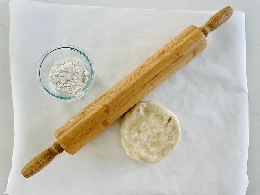 gluten-free pie dough disk (about 5" in diameter), rolling pin and small bowl of dusting flour, birds eye view