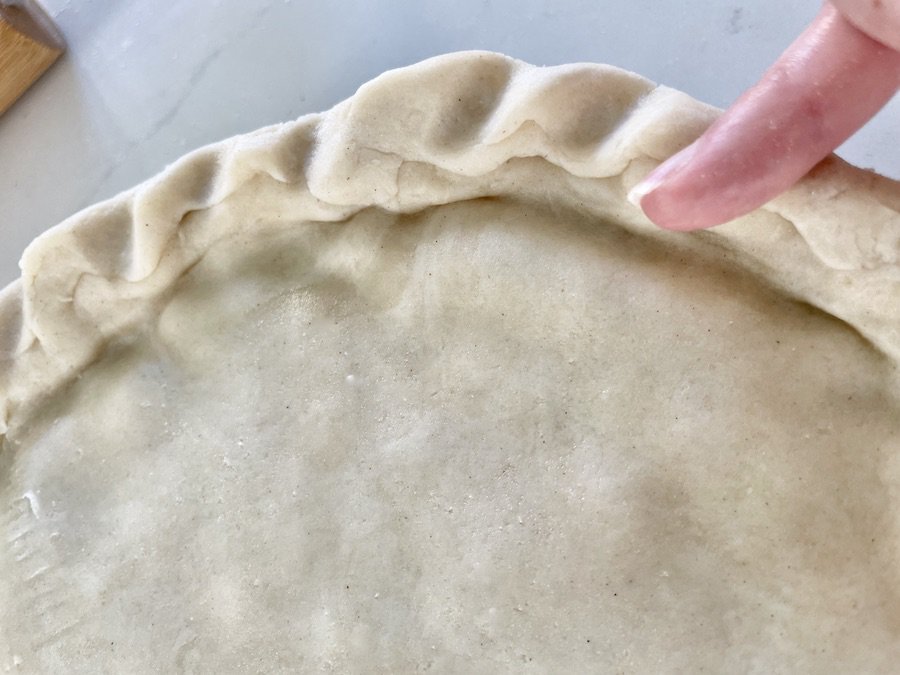 a pinky pressing into the edge of the pie crust to make a decorative edge