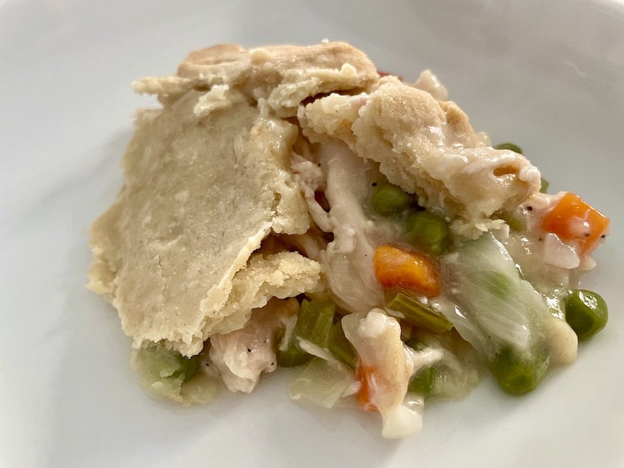 a serving of chicken pot pie with a broken flaky top crust on a white plate