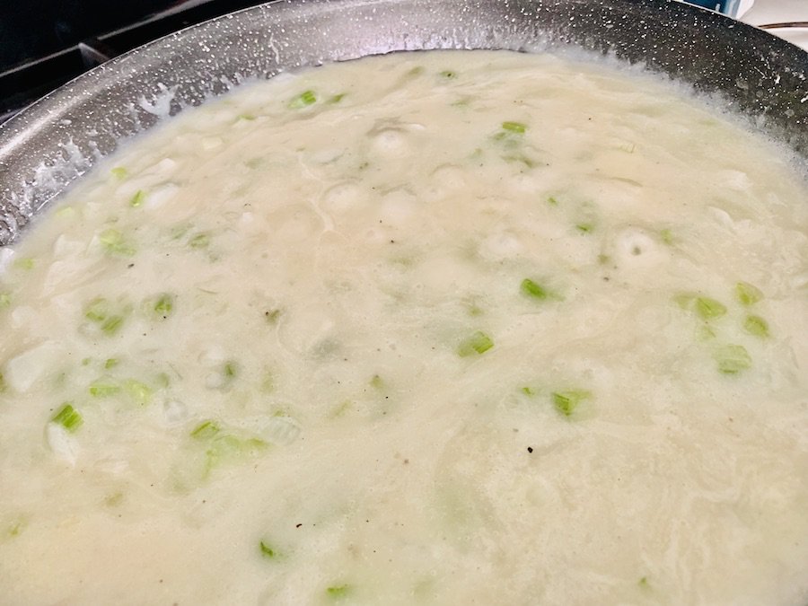 slightly bubbling, thick sauce in a pan with a little color from celery showing