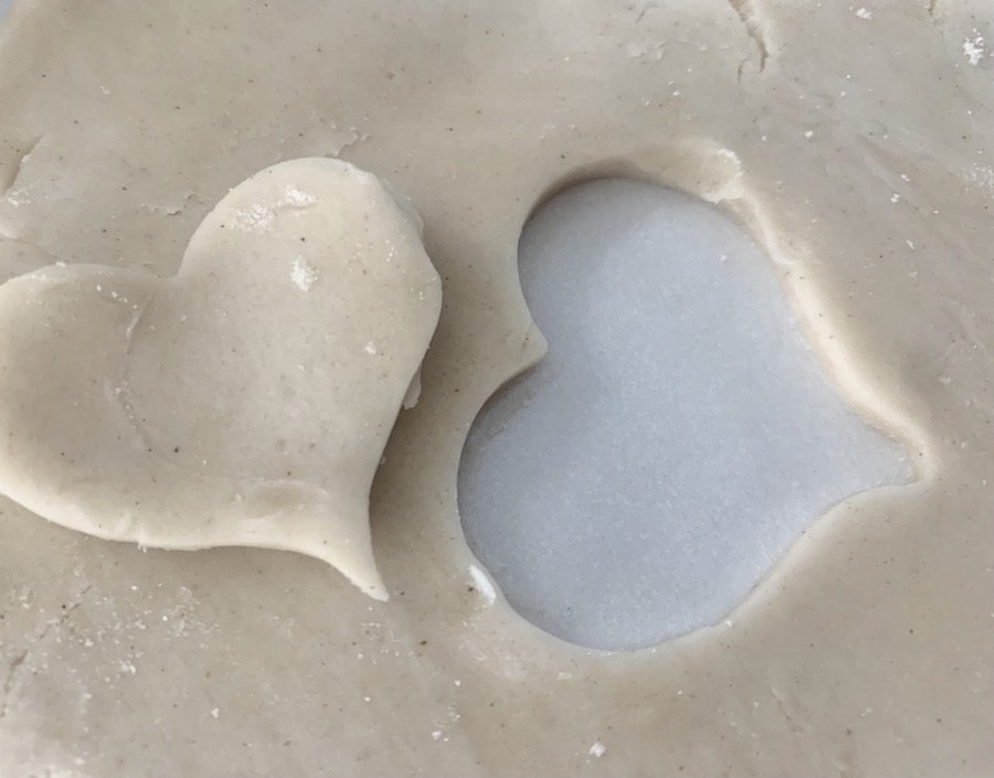 pie crust dough on counter with a heart shape cut out, the cut-out heart is resting on the dough next to the heart-shaped hole