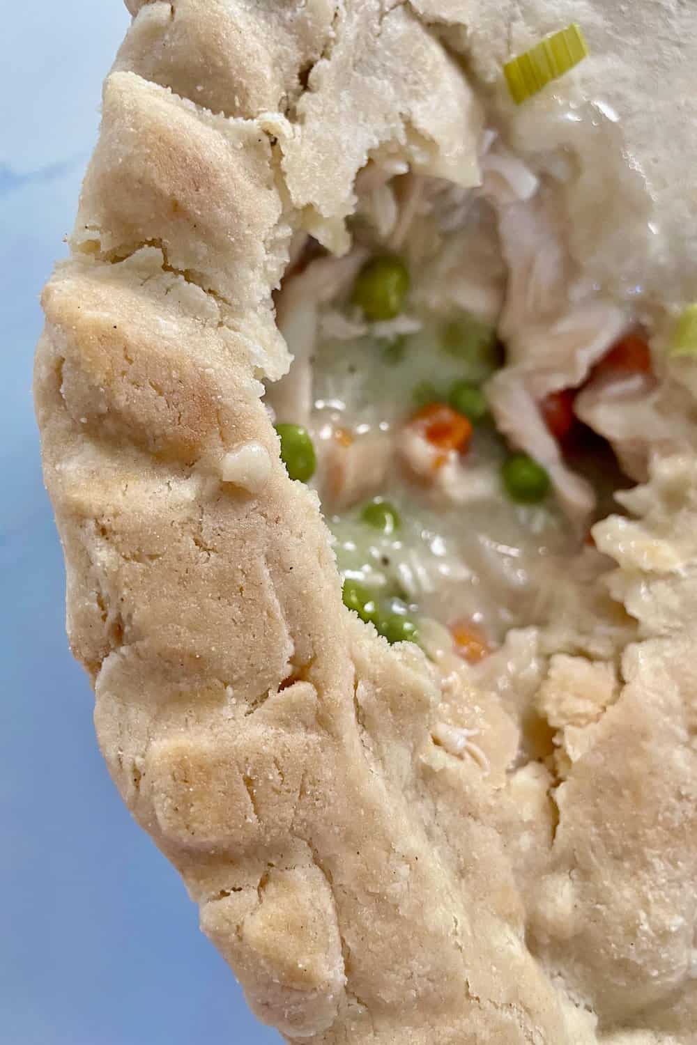 edge of gluten-free chicken pot pie showing golden brown ridged edge and piece of the crust missing to show the filling