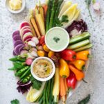 a crudite platter with two small dip bowls in the center and lots of colorful vegetables fanning out from the dips, almost like a sunburst