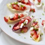 strawberry slices and cheese resting in endive bowls, on a white plate