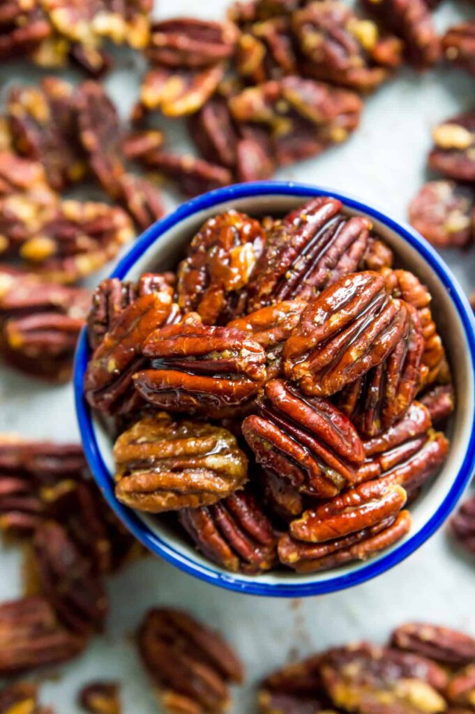 a small bowl of glazed pecans with more pecans (blurry) in the background