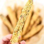 a hand holding up one zucchini fries, with a bunch more in the background